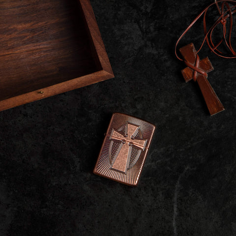 Lifestyle image of Armor Deep Carve Cross Design Antique Copper Windproof Lighter laying flat with a wooden box and cross