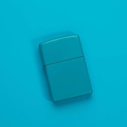 Lifestyle image of Classic Flat Turquoise Windproof Lighter laying on a turquoise surface