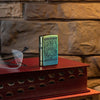 Lifestyle image of John Smith Gumbula Bird High Polish Teal Windproof Lighter standing on a red book with glasses laying next to it